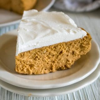 A slice of Instant Pot Pumpkin Cheesecake served on a stack of two white dessert plates set in front of the remaining Instant Pot Pumpkin Cheesecake
