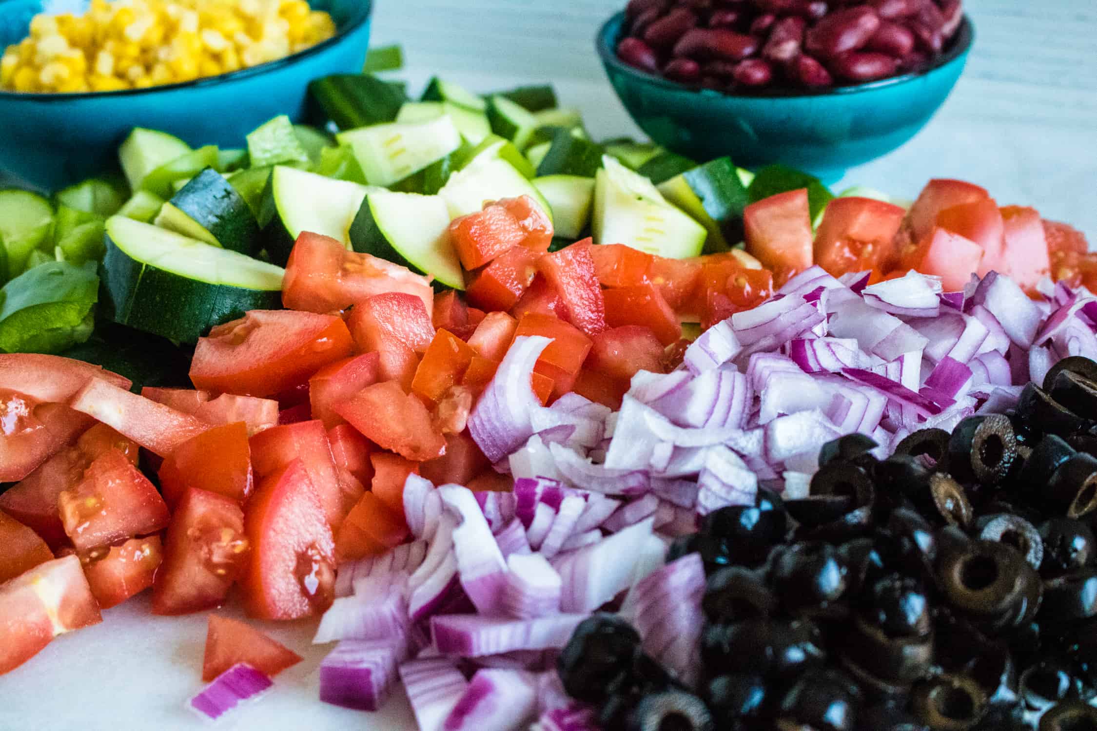 Diced tomato, red onion, olives and zucchini with a bowl of red beans corn beside