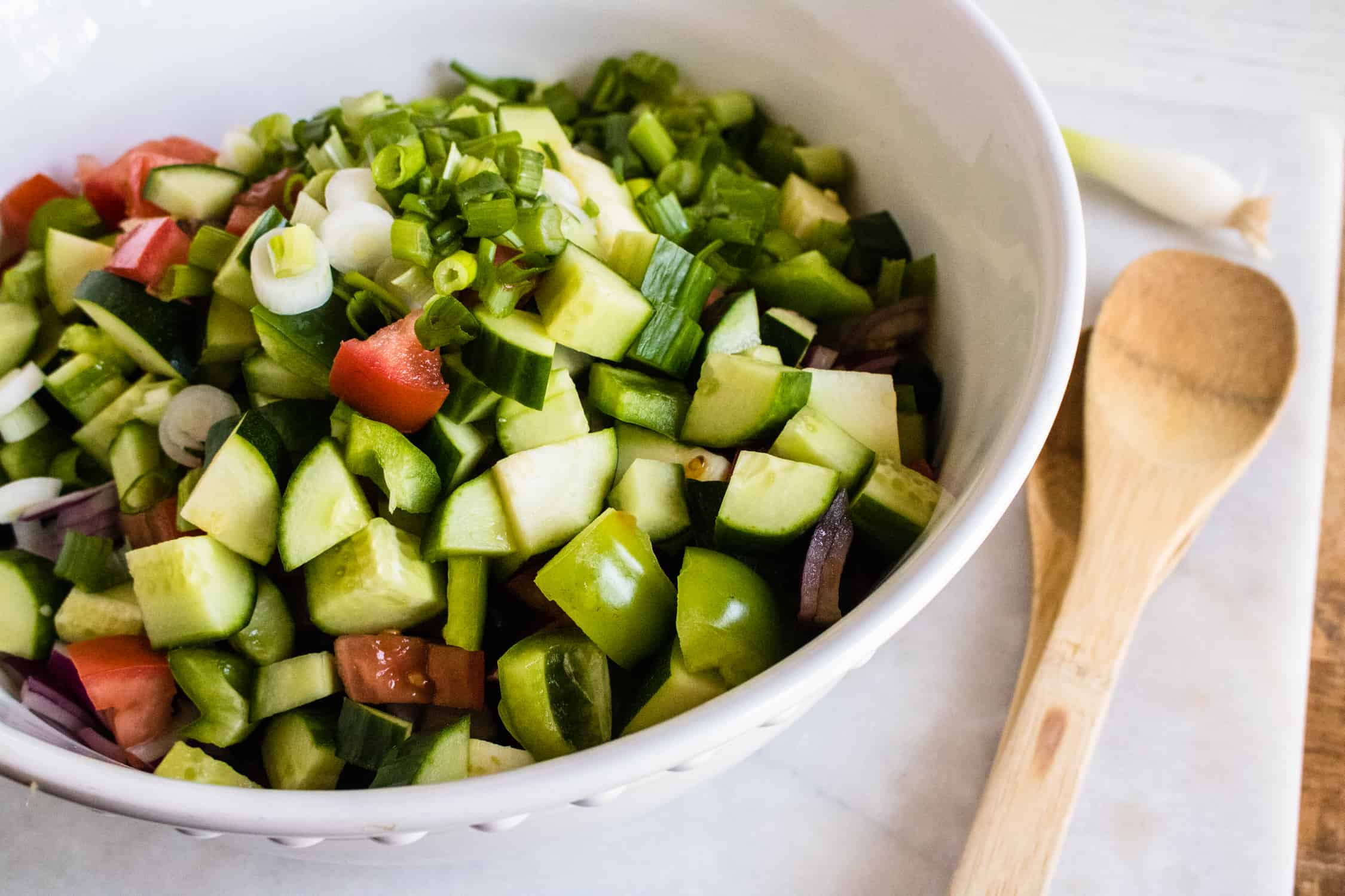 Chopped zucchini, tomatoes, olives, red and green onions mixed together in a large bowl
