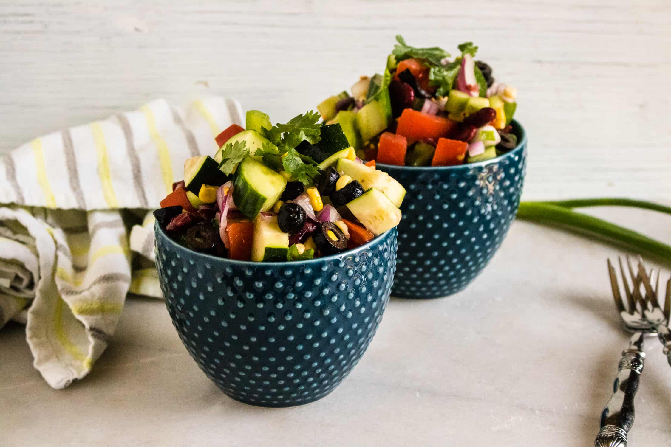 Picnic salad served in two blue bowls with forks and a kitchen towel beaide
