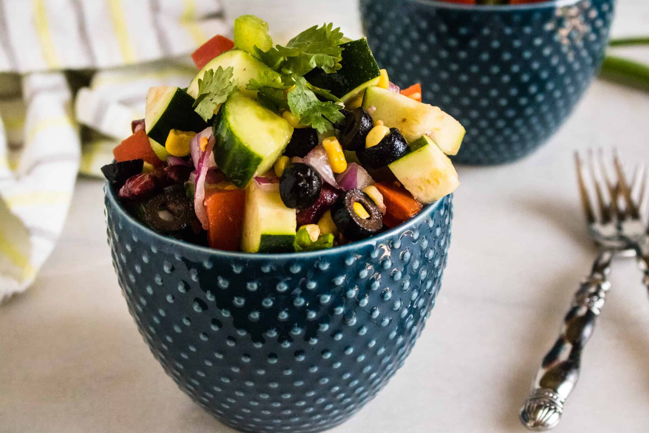 Picnic salad served in a blue dotted bowl with forks and a striped kitchen towel beside