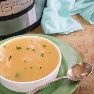 Completed Instant Pot Turkey Gravy in a white serving bowl set on top of a green platter with a silver ladle in front of the Instant Pot and blue cloth napkin