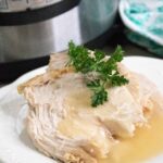 One serving of Instant Pot Turkey on a white plate and set in front of the Instant Pot