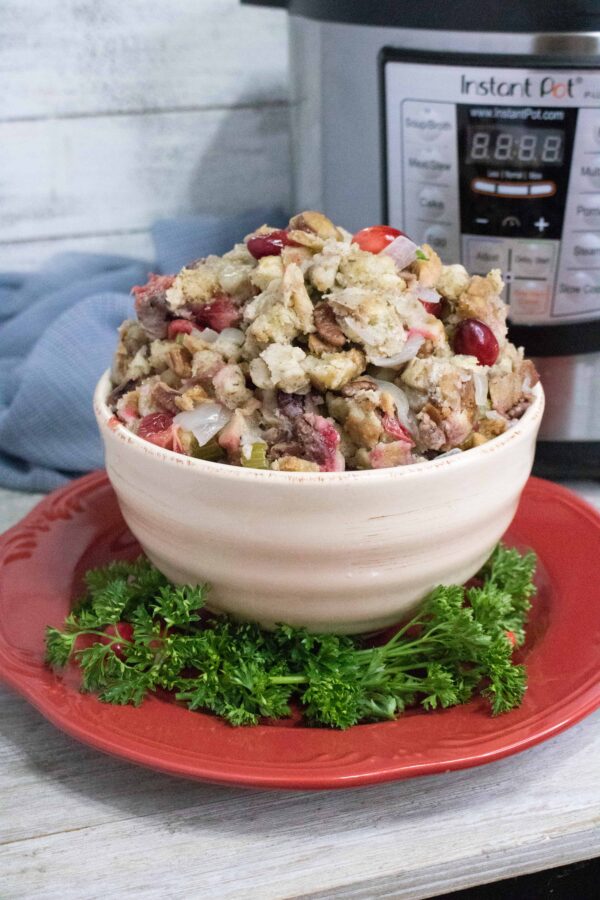 Instant Pot Cranberry Pecan Stuffing in a white bowl set on a red serving plate in front of the Instant Pot