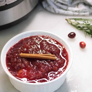 Instant Pot Cranberry Sauce in a white serving bowl and garnished with a cinnamon stick