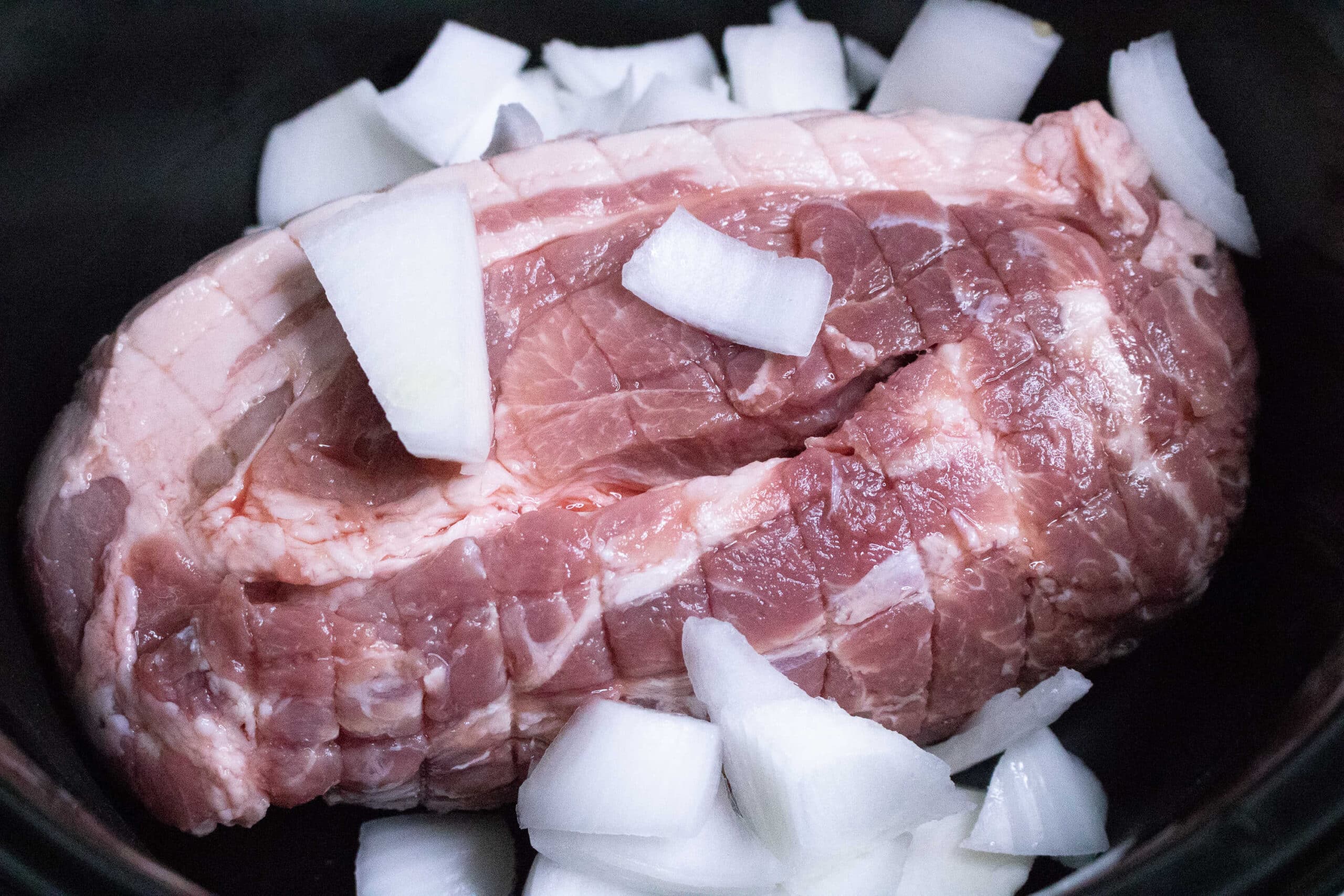 Pork roast for Slow Cooker Pulled Pork sitting in slow cooker with chopped onions on top