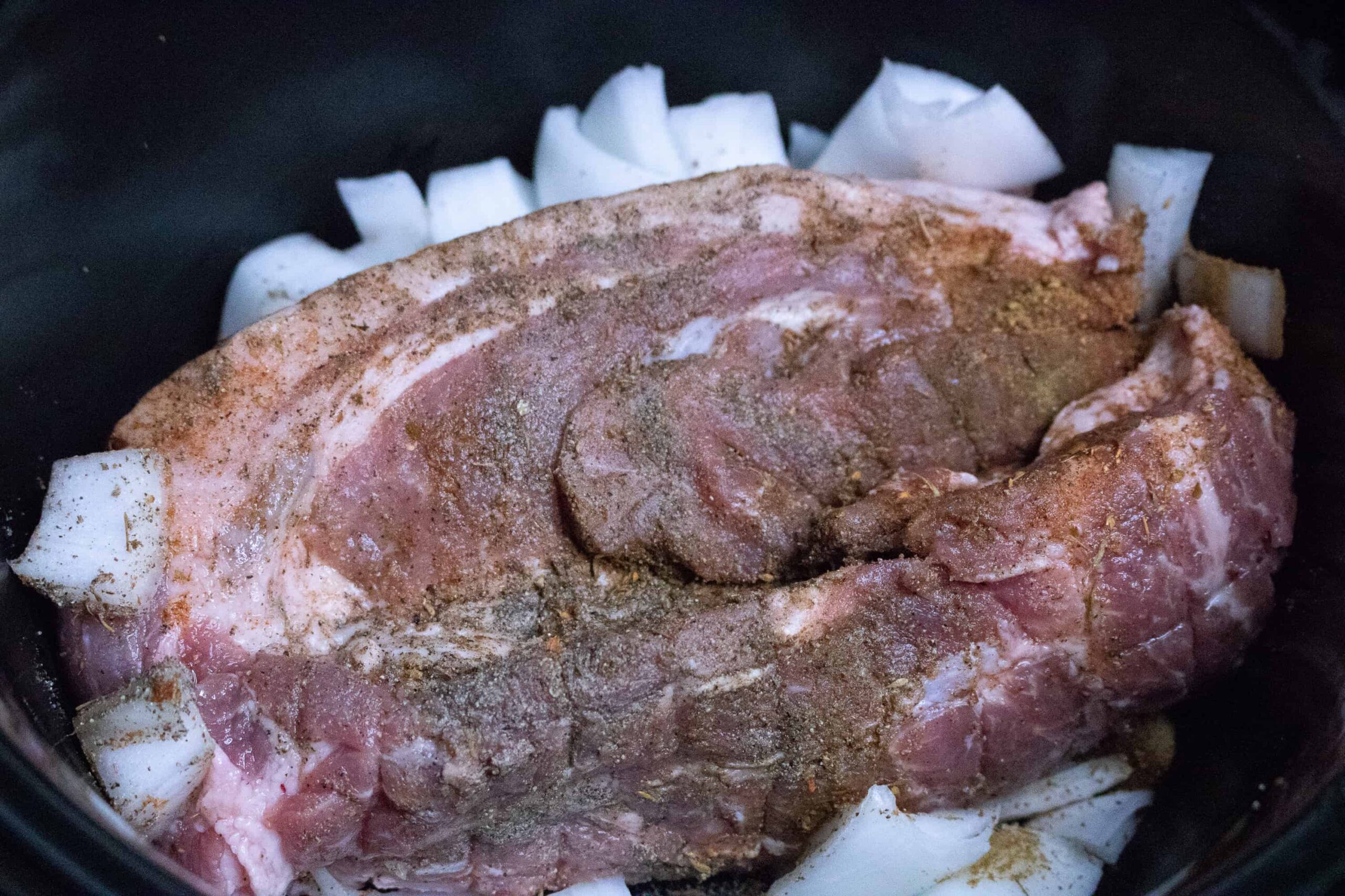 Pork roast for Slow Cooker Pulled Pork sitting in slow cooker with chopped onions and seasonings on top