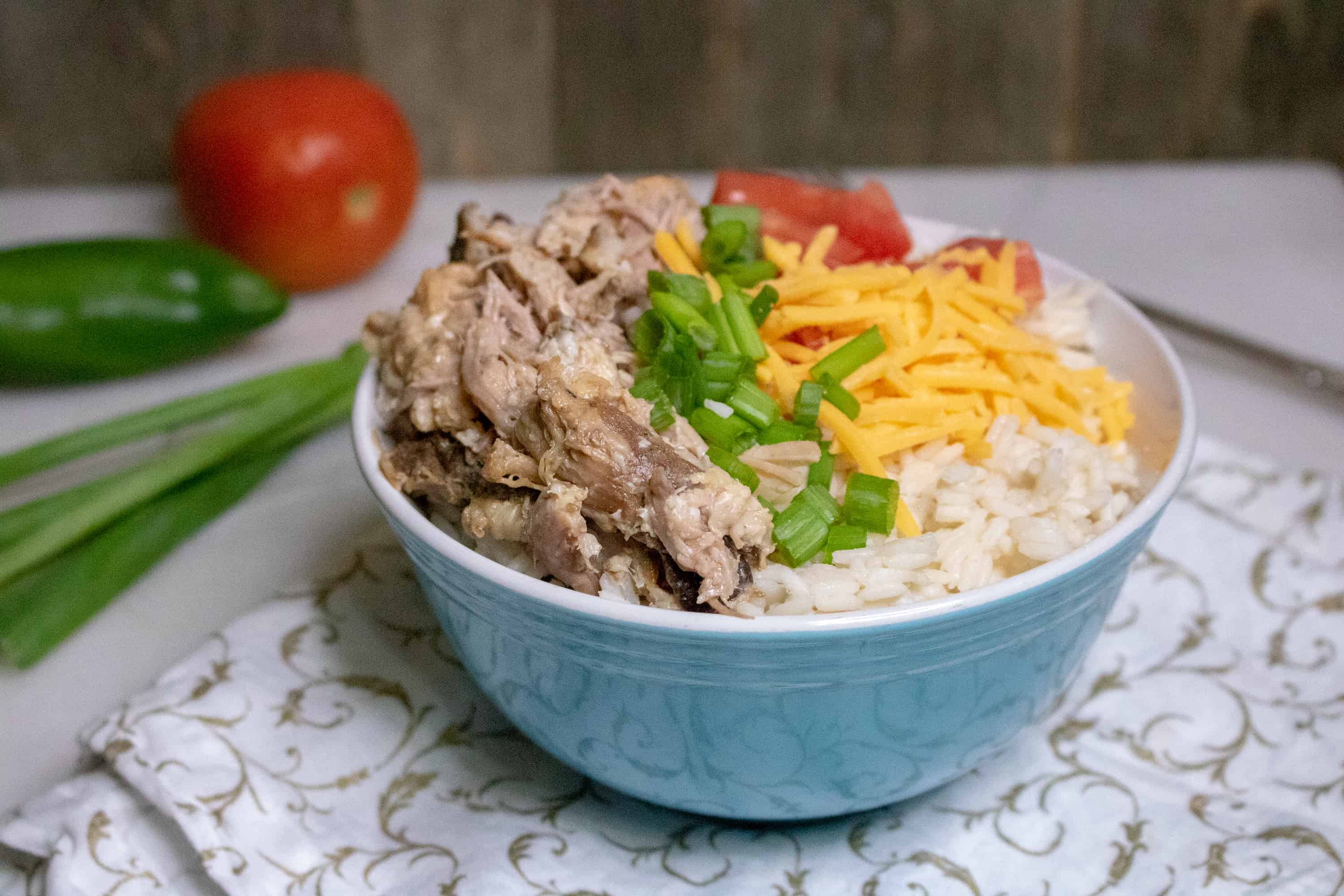Slow Cooker Pulled Pork served with rice, cheese, green onions and tomatoes in blue ceramic bowl.