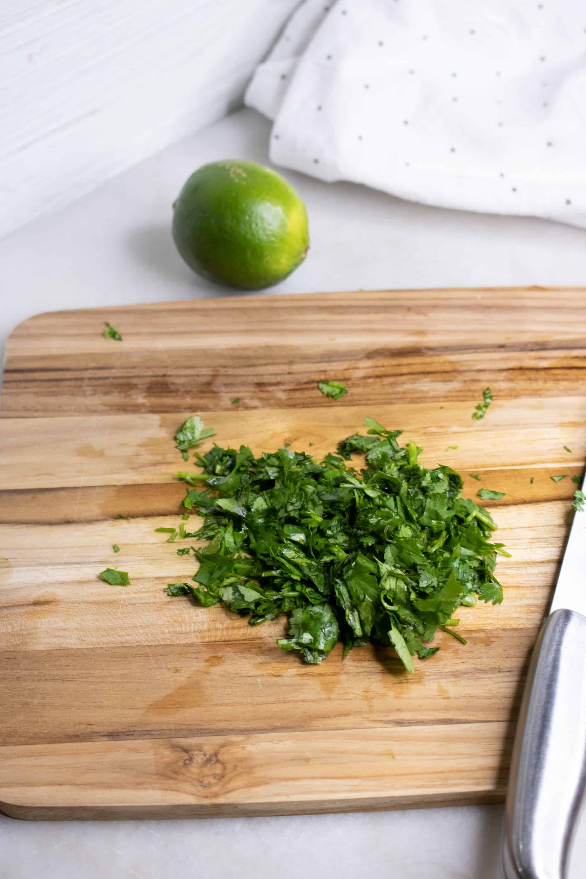 Wooden cutting board with chopped cilantro on it and lime in background for Cilantro Lime Cauliflower Rice
