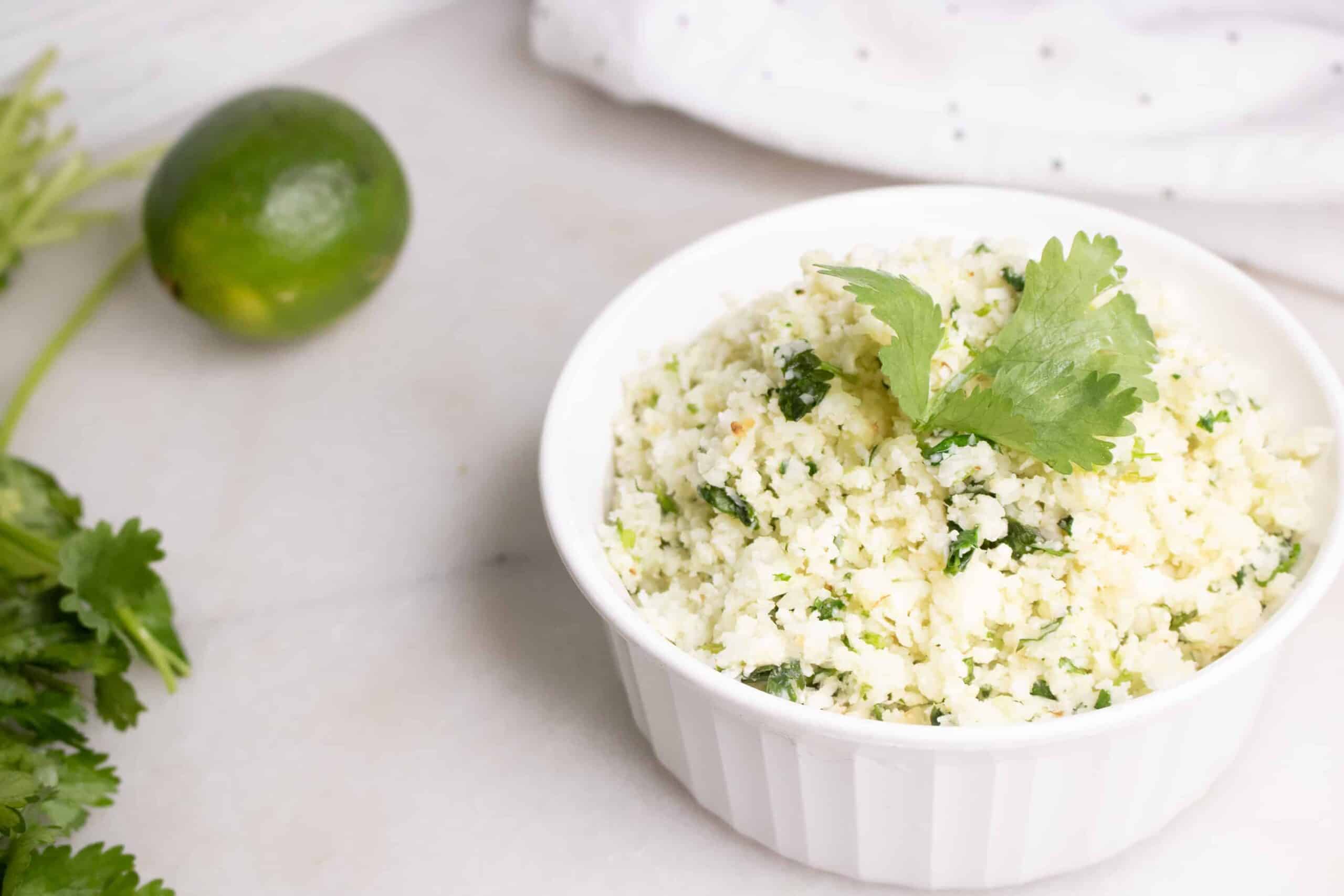 Cilantro Lime Cauliflower Rice in white corning ware casserole with lime in background