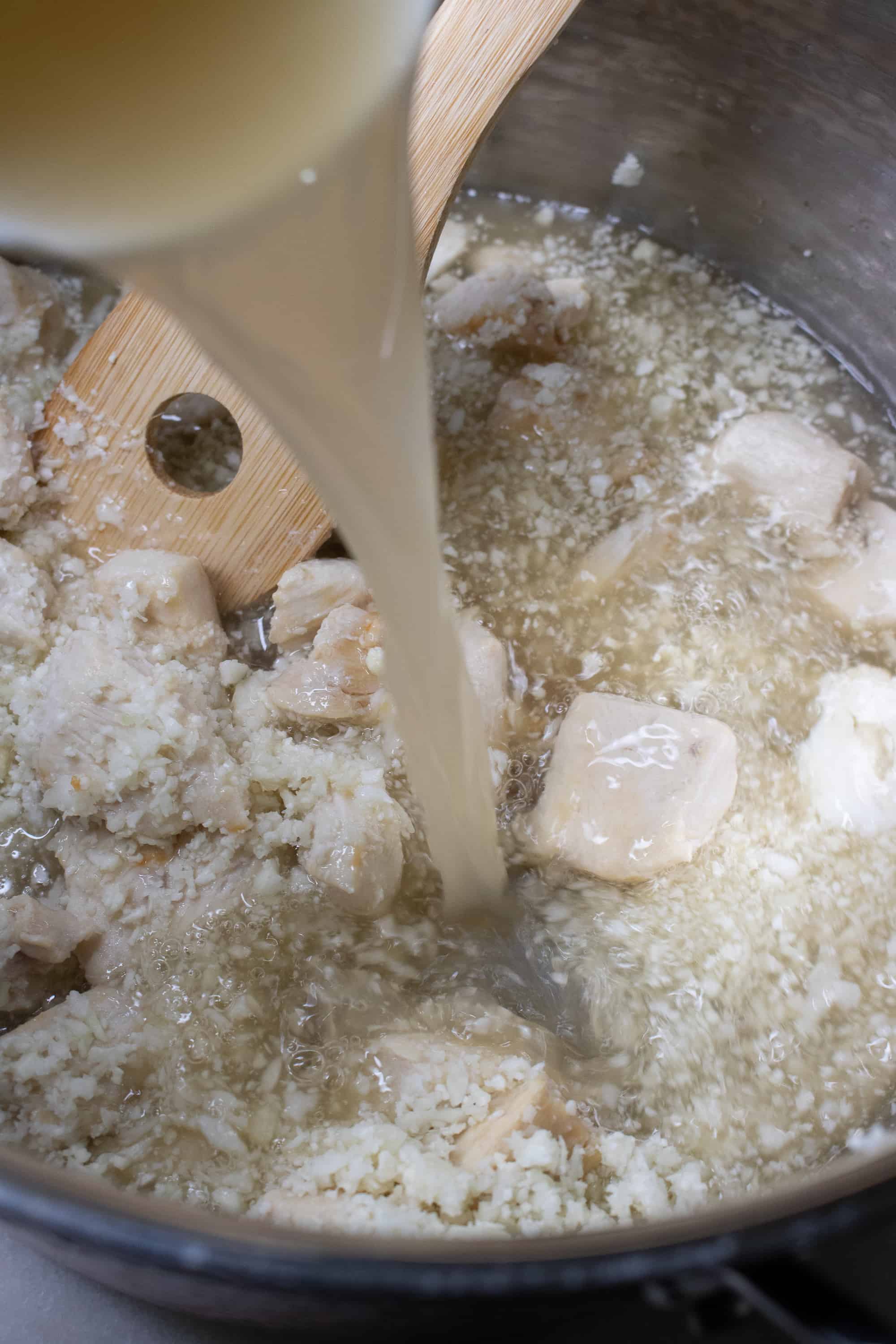 Coconut milk being poured into the cooking pot with the chicken and cauliflower rice for Curry Chicken and Cauliflower Rice soup