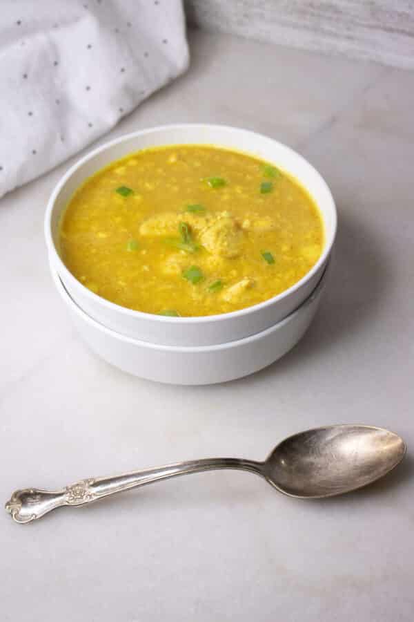 Curried chicken and cauliflower rice soup in a white bowl with a vintage silver spoon