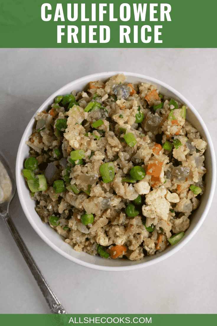 top down view of a serving of cauliflower fried rice in a white bowl next to a silver spoon