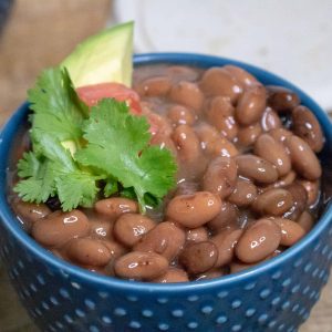 Slow Cooker Pinto Beans served in a blue ceramic dish and topped with tomato, avocado and cilantro