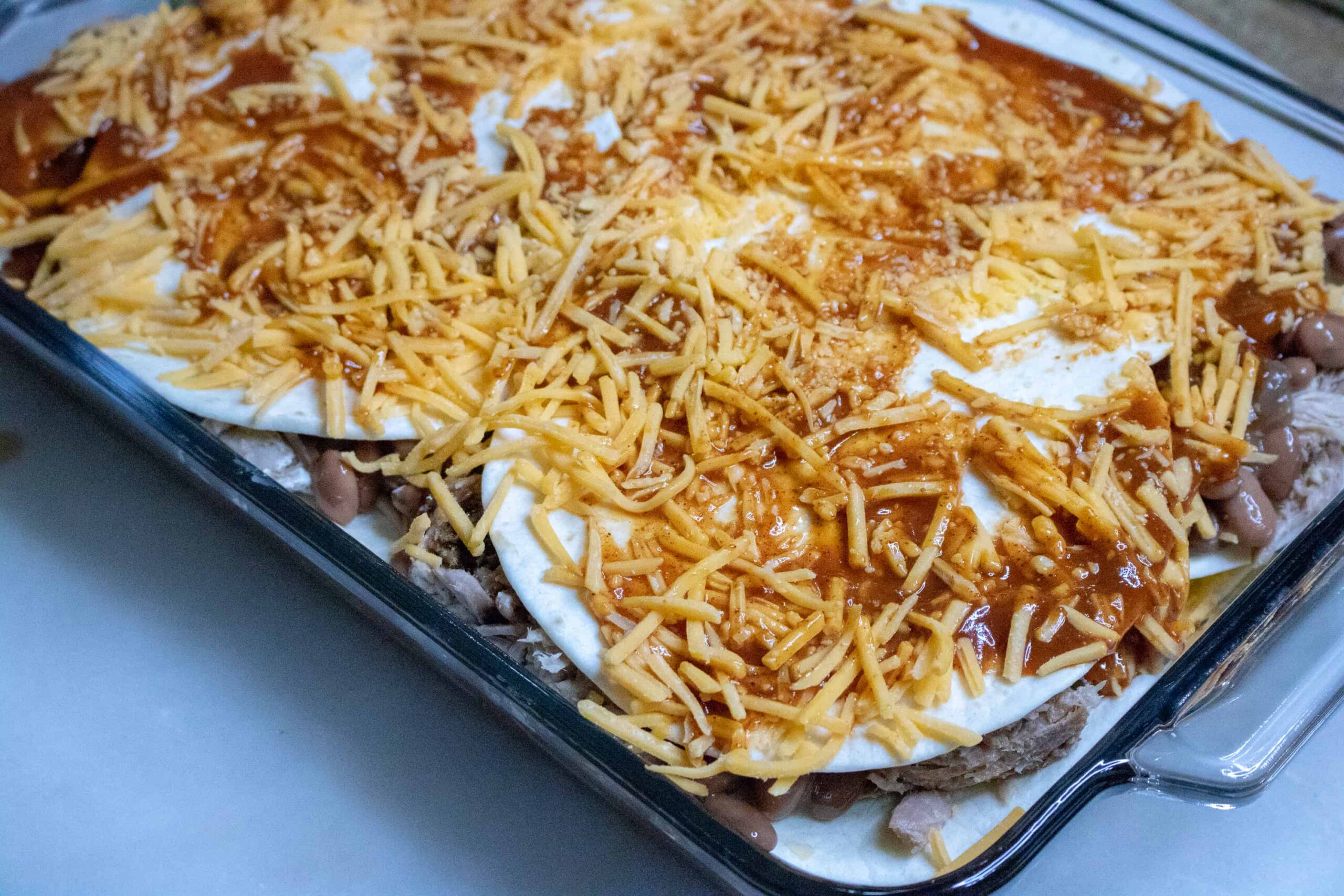 Shredded cheese for Pork Enchilada Casserole on top of other ingredients.