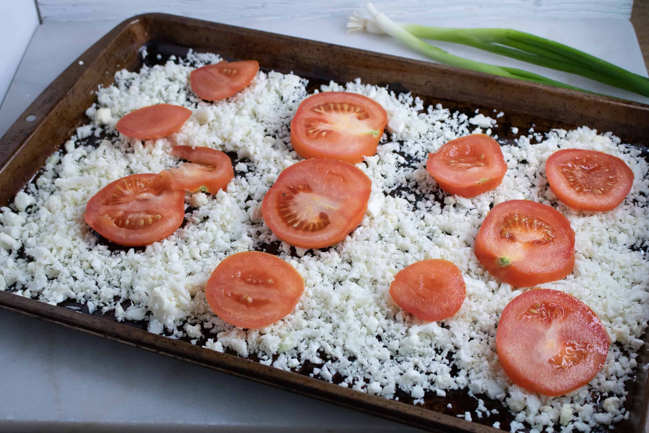 Cauliflower rice and tomato slices on a baking sheet