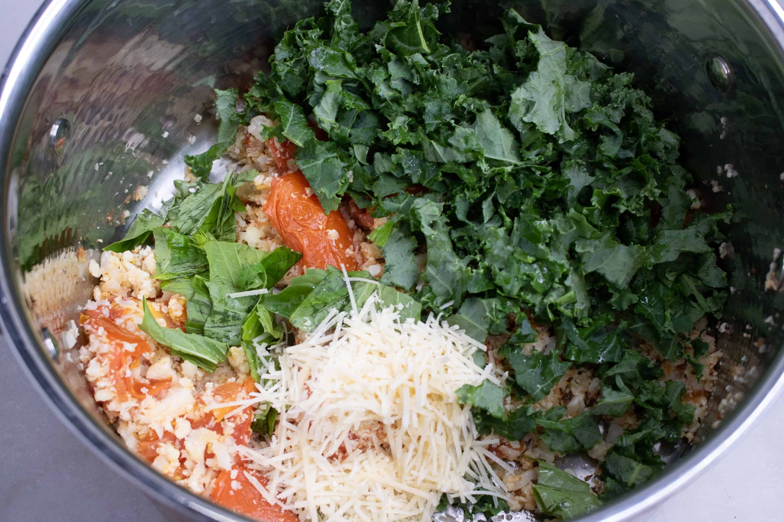 Roasted cauliflower rice, roasted tomatoes, chopped kale, shredded parmesan and fresh basil in a pot