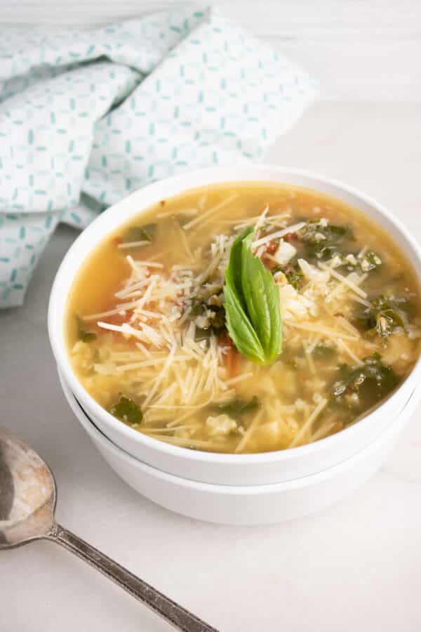 Roasted tomato and cauliflower rice soup in a white bowl topped with shredded Parmesan and a fresh basil leaf