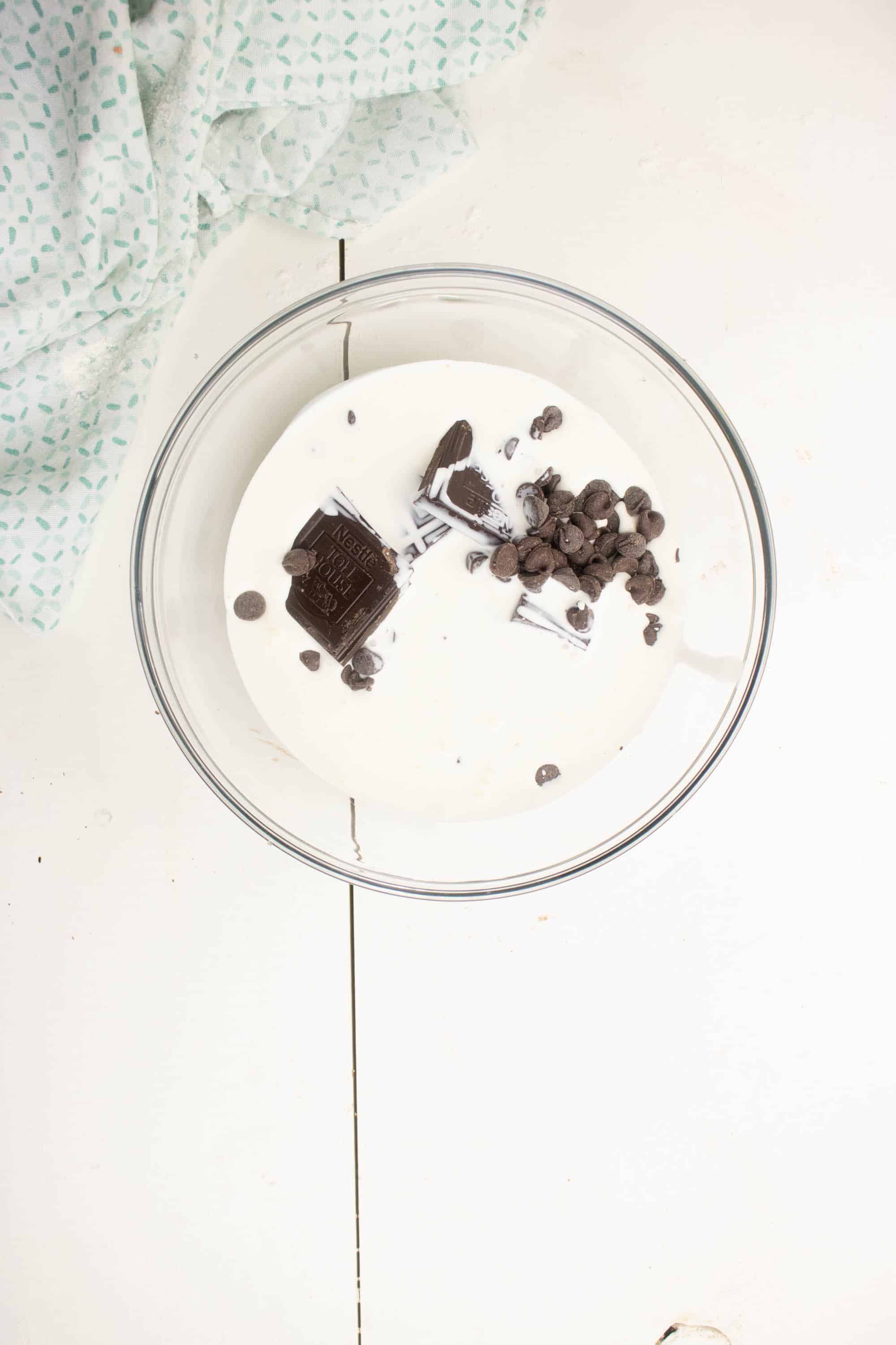 Dark chocolate pieces, semi-sweet chocolate chips and heavy cream for Dark chocolate brownie ganache in glass bowl 