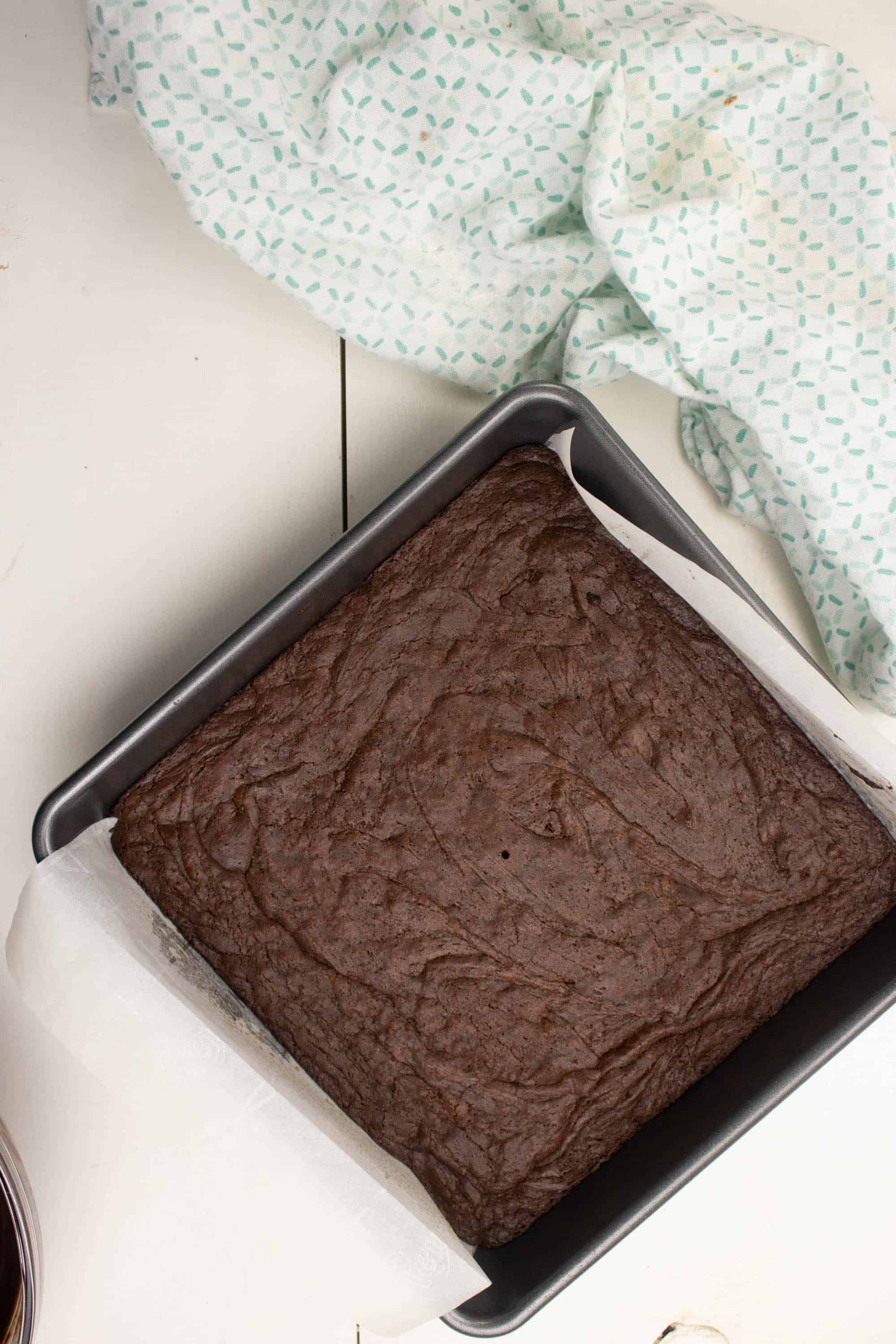 Silver baking pan lined with parchment paper with baked Dark chocolate brownies in it.