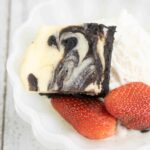 Permalink to: Cheesecake Brownies – Easy Cheesecake Brownies Recipe One serving of Cheesecake Brownies served in a white scalloped bowl with strawberries and whipped cream