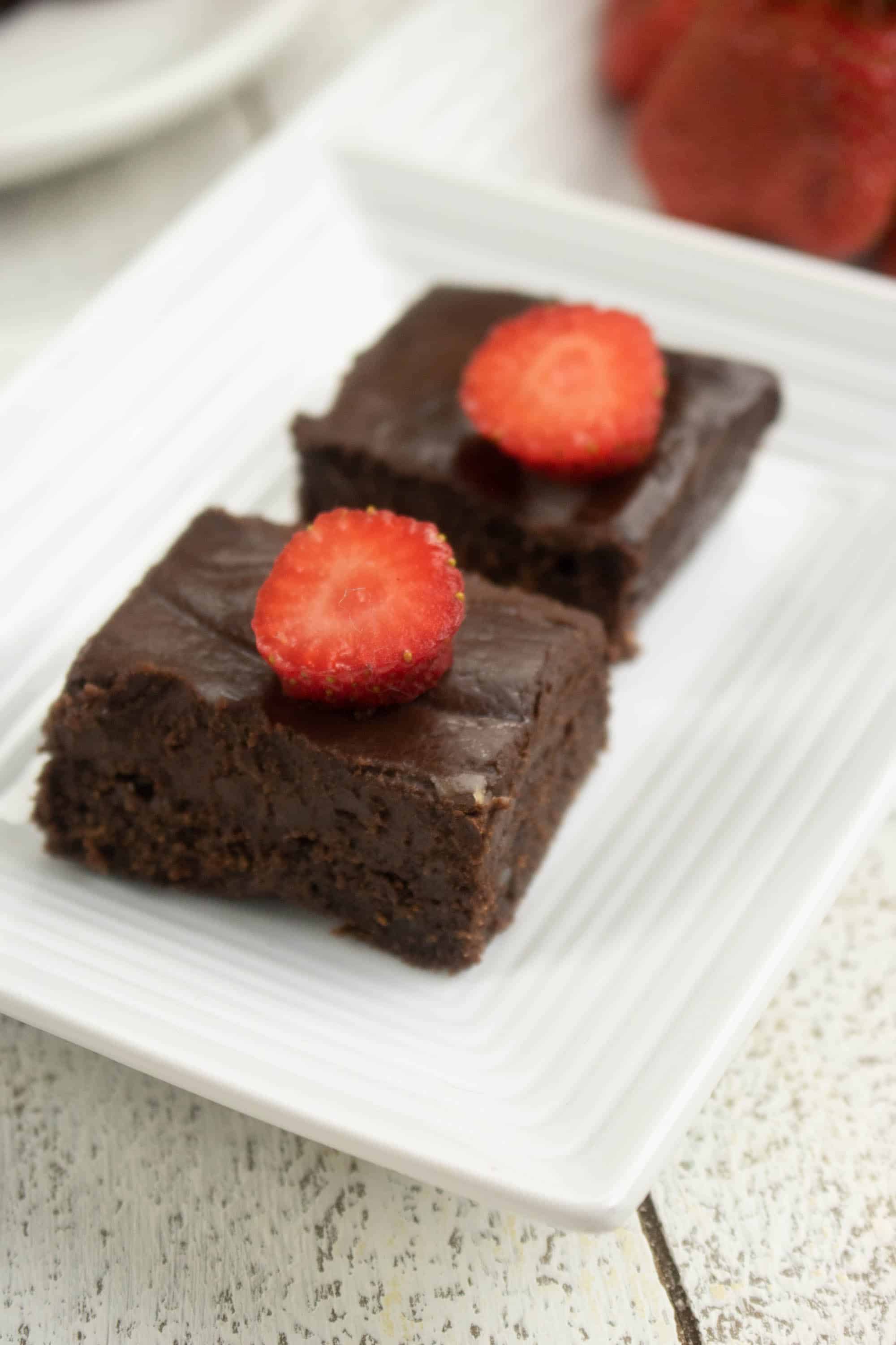 2 dark chocolate brownies with a strawberry slice on each on top of a white plate
