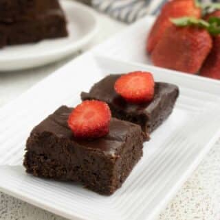 2 dark chocolate brownies on white plate with strawberry slices on top