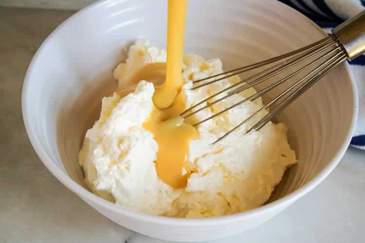 whipped cream in a white bowl with sweetened condensed milk being poured over it