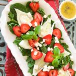 Permalink to: Strawberry Fennel Salad with Homemade Vinaigrette top down view of strawberry fennel salad served on a white oval platter with a cup of homemade dressing on the side