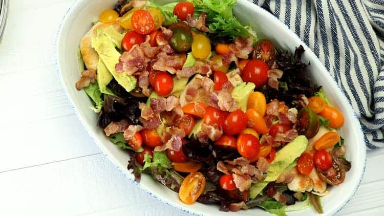 overhead shot of salad with tomatoes and bacon in white oval dish