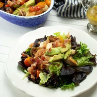salad with chicken and bacon atop lettuce on a white plate