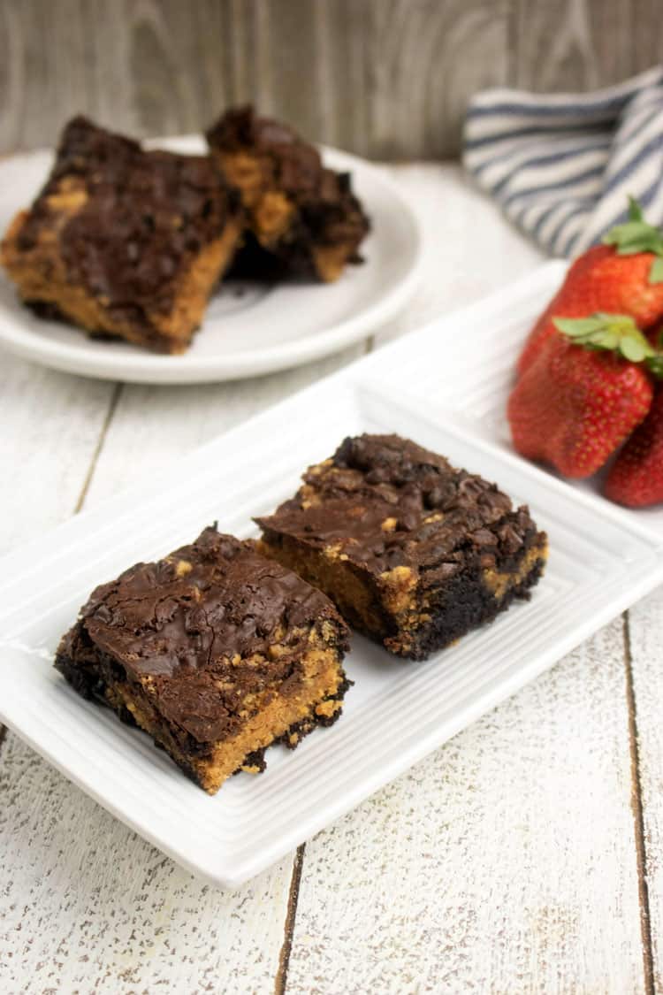 peanut butter brownies on white plate with strawberries in the background