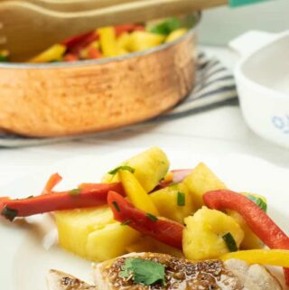 plated healthy pork chop recipe on white plate with pineapples and yellow and red bell peppers