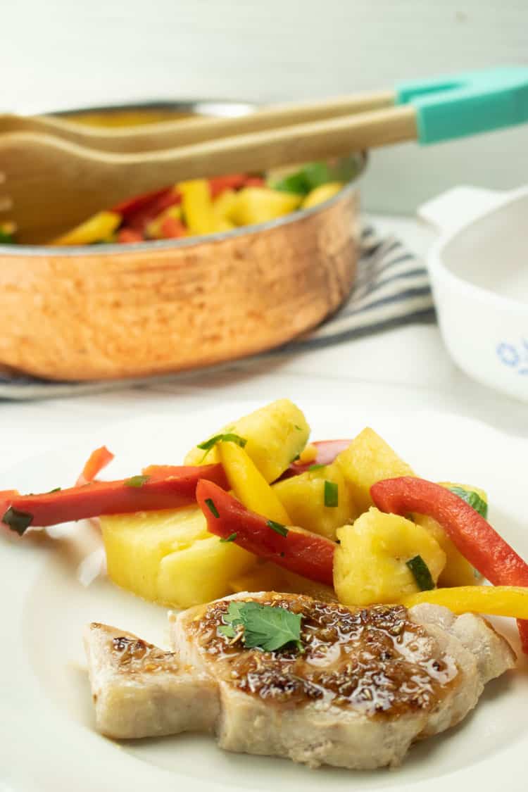 plated healthy pork chop recipe on white plate with pineapples and yellow and red bell peppers