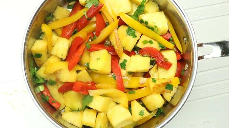 pan with pineapple chunks mixed in with sliced yellow and red peppers. Chopped parsley is sprinkled over the fruit and vegetables.