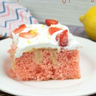 strawberry poke cake with slices strawberries on top, on a white plate with a lemon and colorfully striped napkin in the background