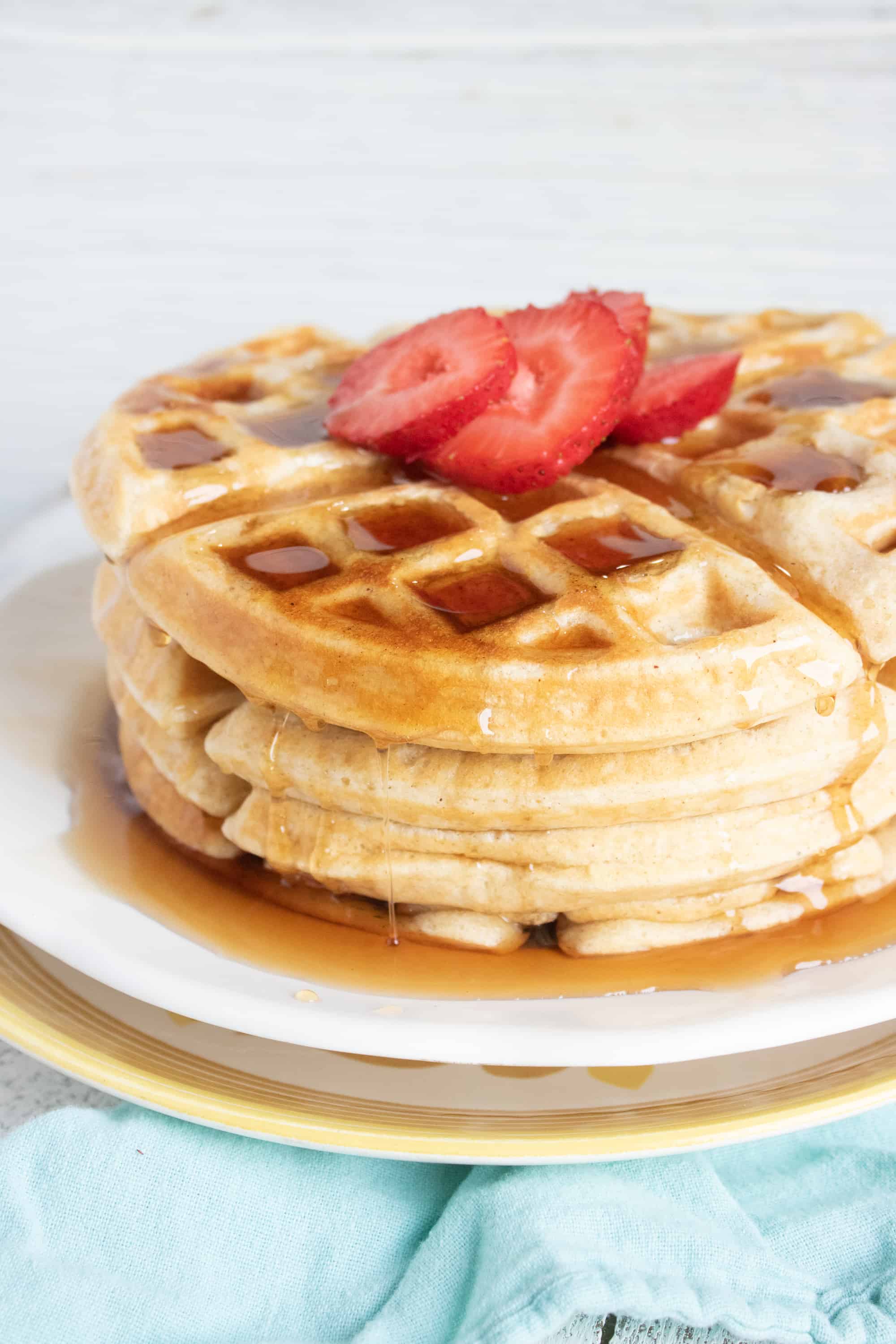 easy belgian waffles on plate covered with syrup and strawberries