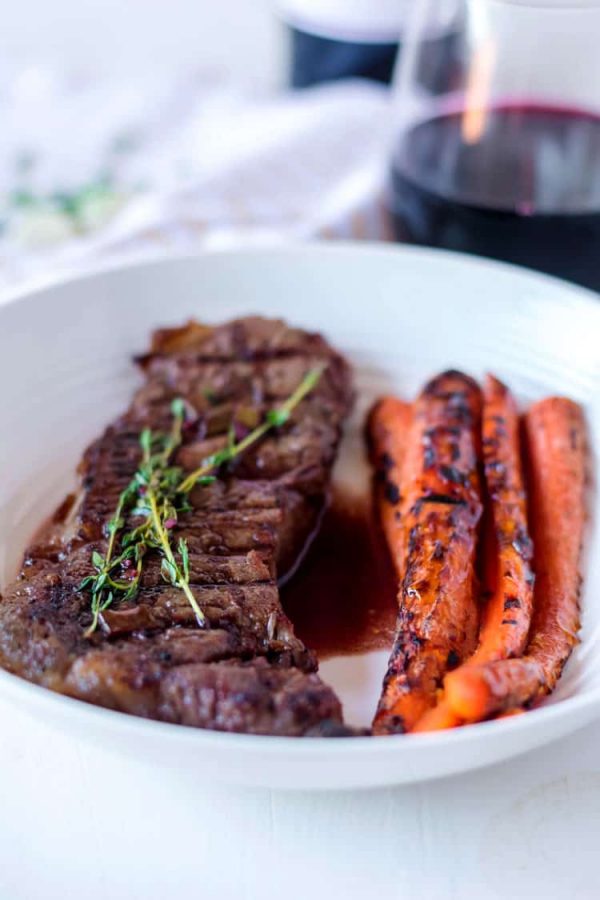 grilled steak being served with carrots in a white dish