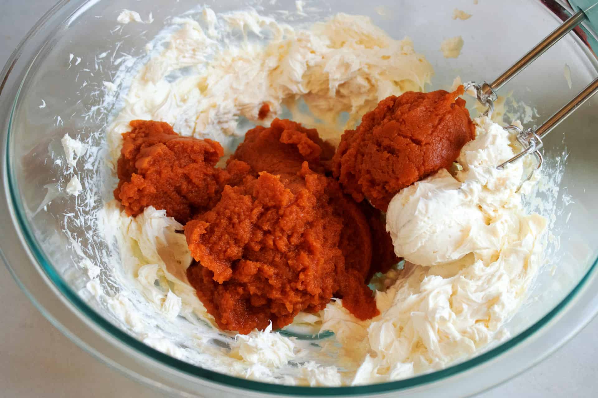 Pumpkin puree added to whipped cream cheese in a glass bowl for the pumpkin cream cheese filling