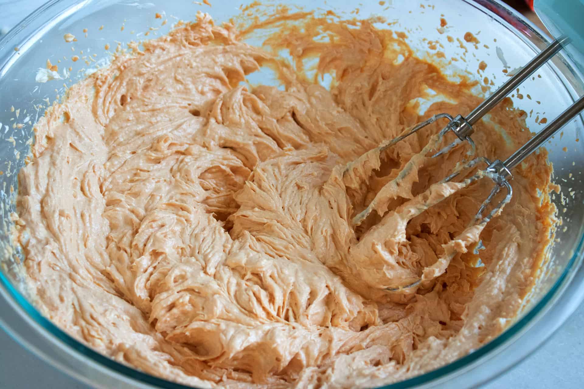 Pumpkin cream cheese filling being whipped with a hand mixer in a glass bowl