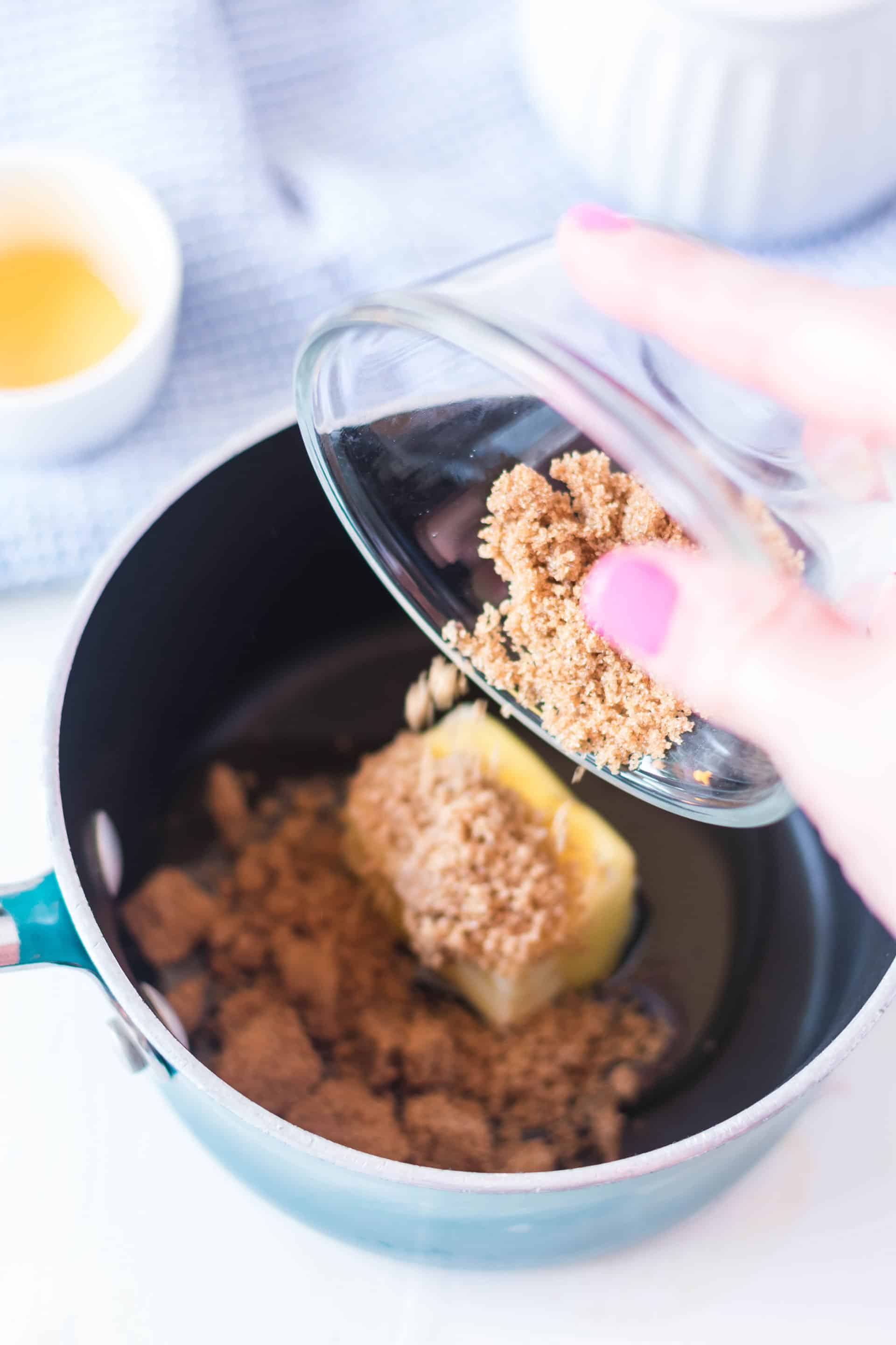 pouring brown sugar into a pan with butter and honey 