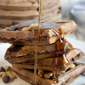 chocolate waffles on a white plate with syrup being poured over them.