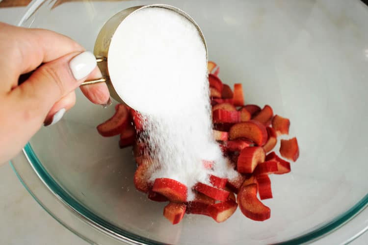 pouring sugar into a bowl with rhubarb