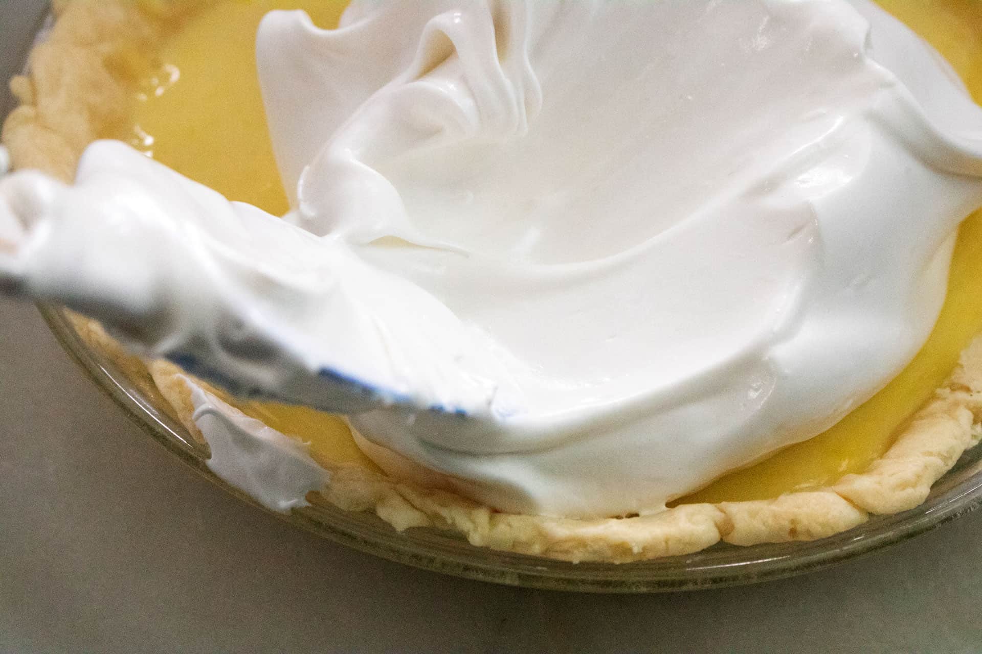 meringue being spread out over lemon cream pie