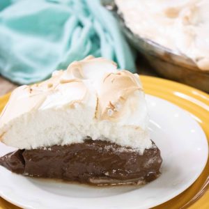 chocolate meringue pie set on white and yellow plates with a blue towel in the background and the pie to the top right