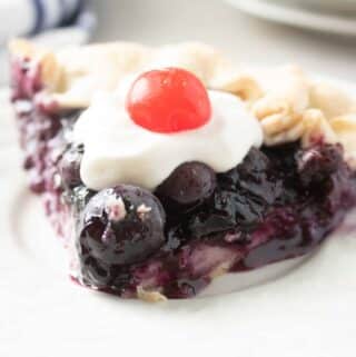 slice of blueberry pie with a cherry on top on a white plate