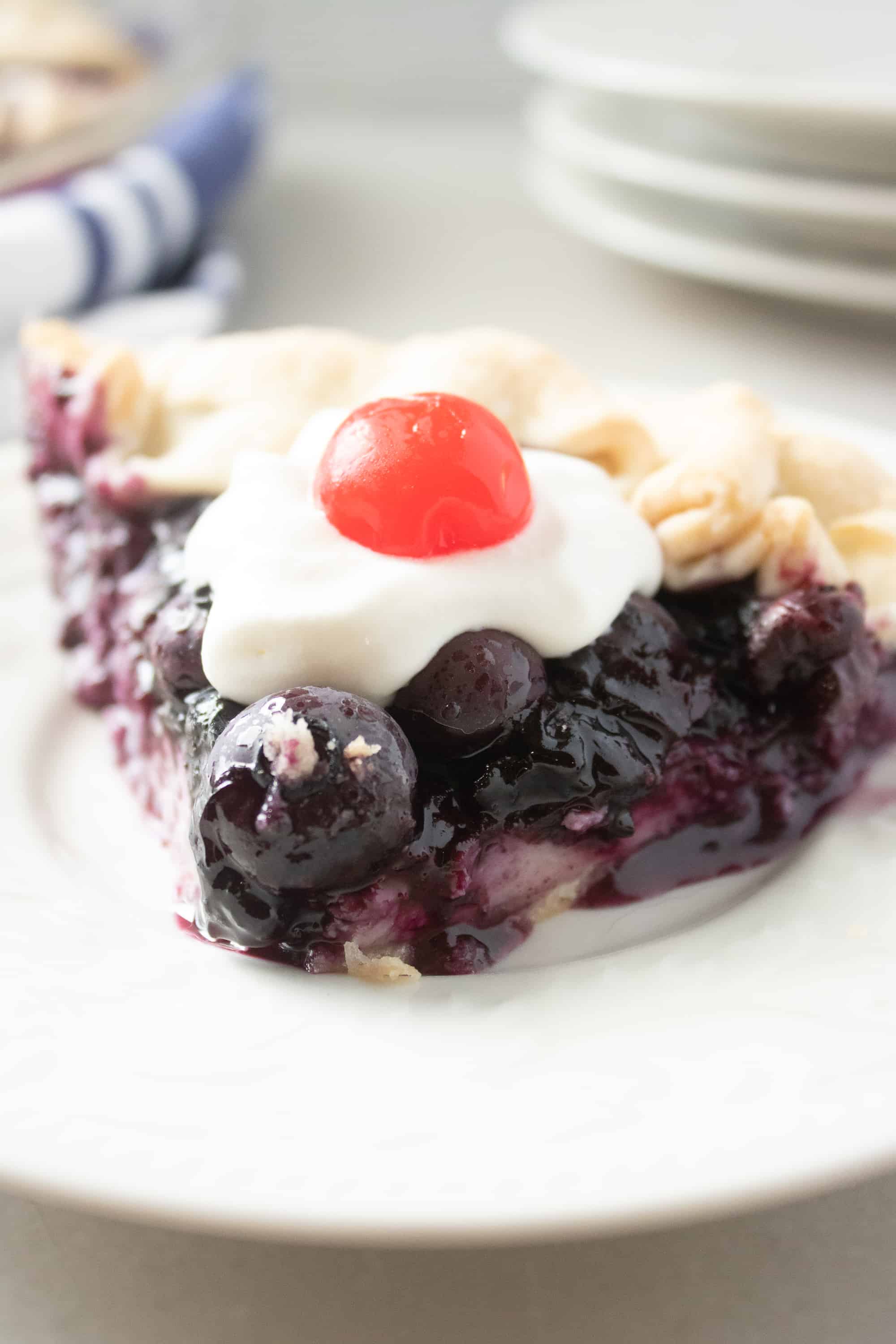 slice of blueberry pie with a cherry on top on a white plate