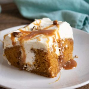 pumpkin poke cake on white plate with blue towel in the background