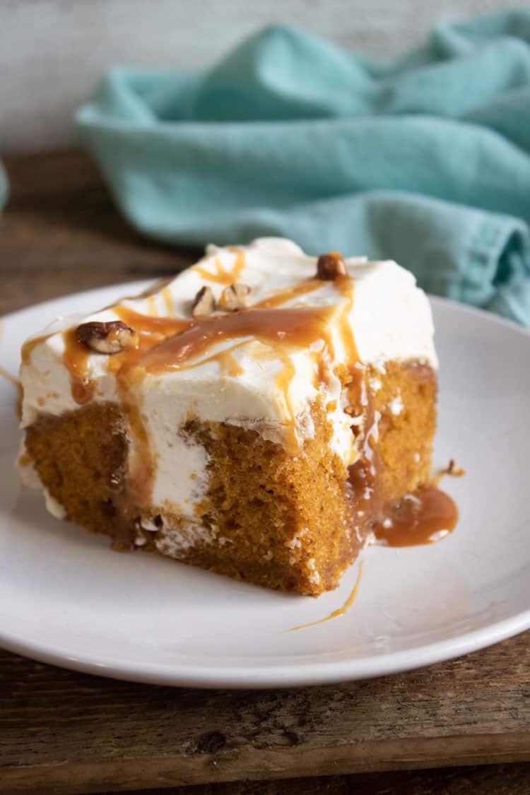 pumpkin poke cake on white plate with blue towel in the background