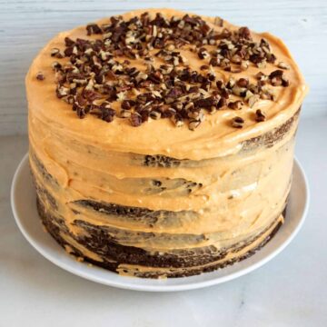 Six-layer chocolate cake with pumpkin cream cheese frosting and chopped pecans on a white cake plate